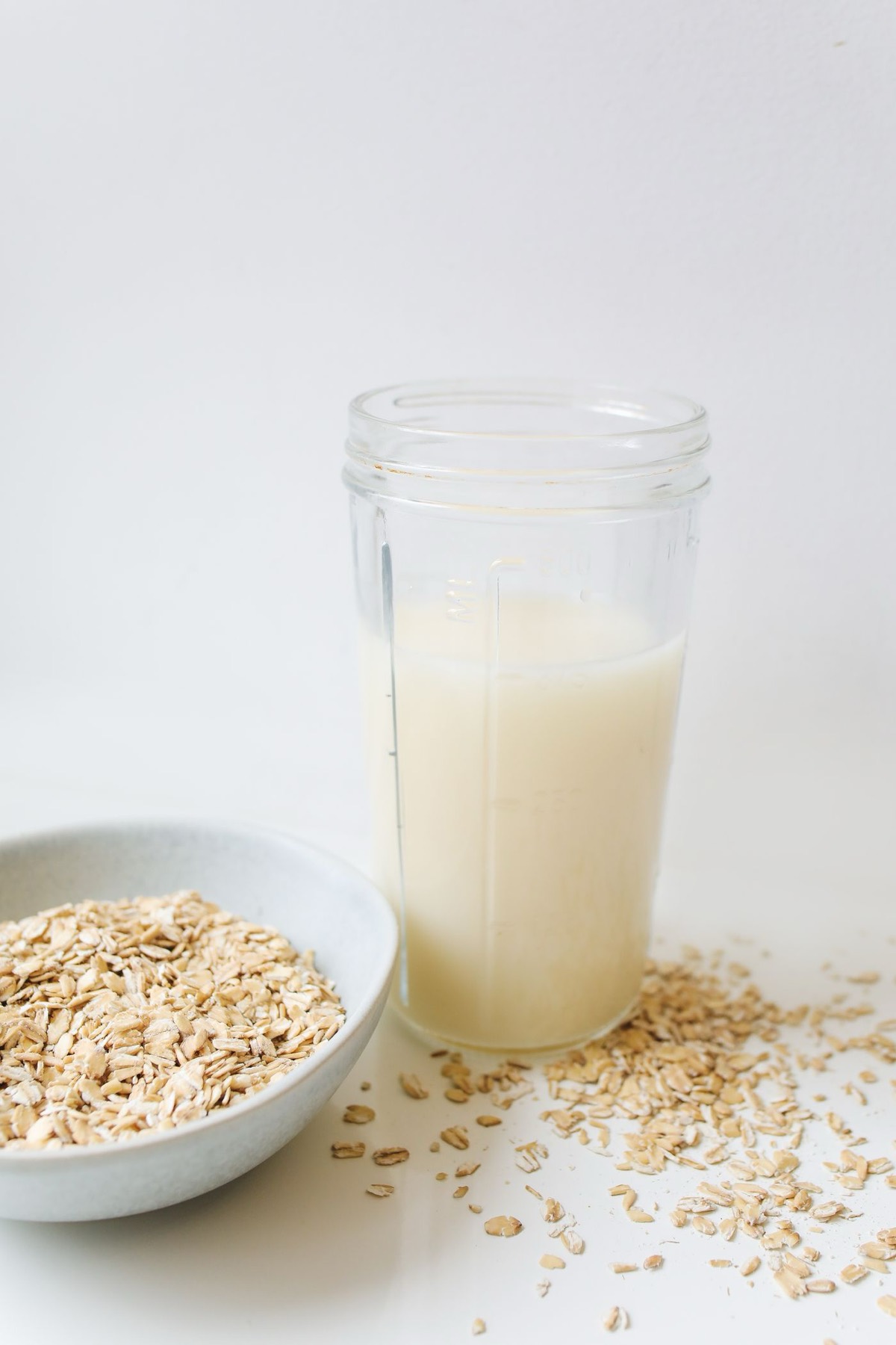 Glas frische Hafermilch neben einer Schale Haferflocken